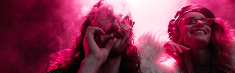 panoramic shot of man smoking marijuana joint near smiling girl in nightclub
