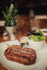 A close up shot of a beef fillet steak with sea salt served on a ceramic plate with salad and sauce. Concept of restaurant, food and culinary.