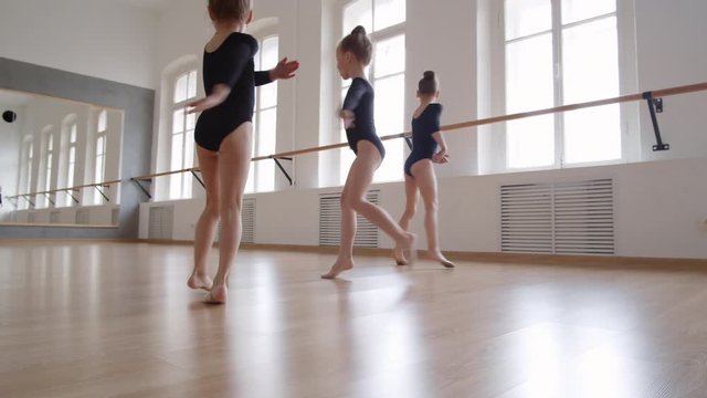 Wide shot of three little Caucasian girls wearing black leotards dancing together in ballet school