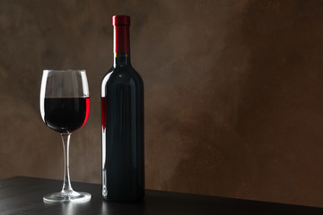 Bottle and glass with wine against brown background, copy space