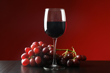 Grapes and glass with wine against red background, copy space