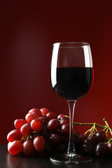 Grapes and glass with wine against red background, copy space