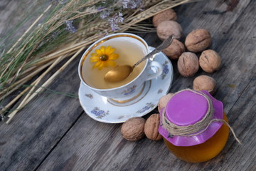 Cup of herbal tea, honey in the pot, sunflower and dry herbs on wooden background, healthy lifestyle