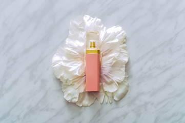   Pink bottle of perfume with flower petals on marble background, top view. Perfumery and floral scent concept. creative trendy flat lay.