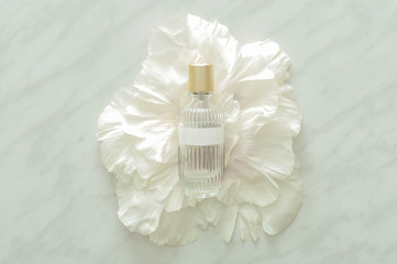 Bottle of perfume with flower petals on marble background, top view. Perfumery and floral scent concept. creative trendy flat lay.