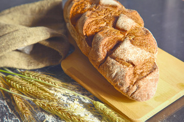 rustic crusty bread and wheat ears on a dark wooden table