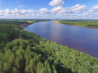 Wooded river banks against a background of individual white clouds in a blue sky. View from above. Vychegda River In Komi Republic, Russia