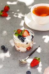 Close up breakfast in jar. Yogurt, granola, strawberries, blueberries with spoon and cup of tea