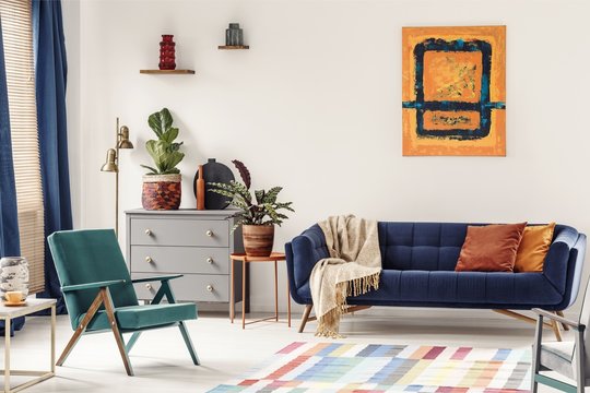 Orange end table with fresh plant standing next to navy couch wi