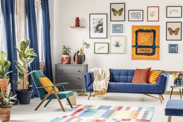 Orange pillow on green armchair near blue couch in colorful livi