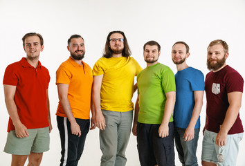 Obraz premium Młodzi mężczyźni ubrani w kolory flagi LGBT na białym tle. Kaukascy mężczyźni w koszulach w kolorze czerwonym, pomarańczowym, żółtym, zielonym, niebieskim i fioletowym. Duma LGBT, prawa człowieka i koncepcja wyboru.