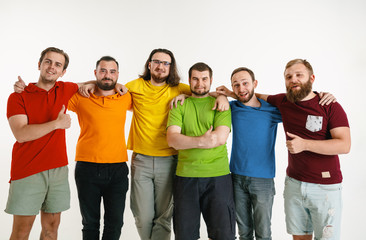 Obraz premium Young men weared in LGBT flag colors isolated on white background. Caucasian male models in shirts of red, orange, yellow, green, blue and purple. LGBT pride, human rights, choice concept. Look happy.