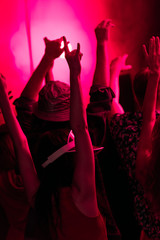 back view of people with raised hands during rave party in nightclub with pink lighting
