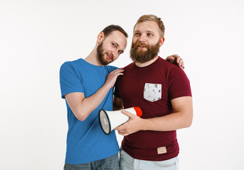 Young men weared in LGBT flag colors on white background. Caucasian male models in bright shirts. Look happy, smiling and hugging. LGBT pride, human rights and choice concept. Holding mouthpiece.