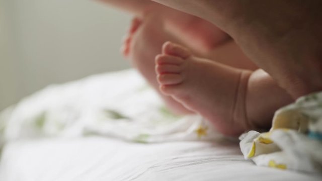 Mother with 2 month child together in bedroom, lying on bed in daylight. Detail view unrecognizable woman gently touch little baby feet and fingers in hand. Conceptual image of maternity.