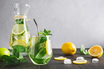 Detox water or lemonade with lemon mint, citrics in glass on wooden table and grey backdrop.