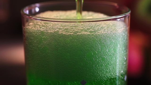 Green estragon lemonade pouring into water glass with lot of bubbles and foam. Full HD 60fps footage with shallow depth and blurring bokeh.