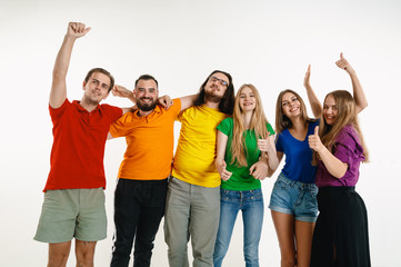 Young man and woman weared in LGBT flag colors on white background. Caucasian models in bright shirts. Look happy together, smiling, hugging. LGBT pride, human rights and choice concept. Celebrating.