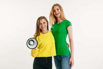 Young women weared in LGBT flag colors on white background. Caucasian models in bright shirts. Look happy, smiling and hugging. LGBT pride, human rights and choice concept. Holding mouthpiece.