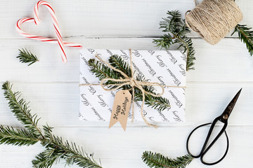 Beautiful Christmas gift with Happy Holidays tag. Decorated naturally with pine tree twigs and twine over a white background with candy canes. Image shot from above.