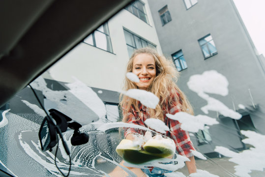 Low Angle View Of Happy Girl Washing Car With Sponge