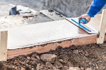 Construction Worker Using Trowel On Wet Cement Forming Coping Around New Pool