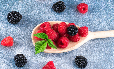 raspberries and blackberries in a wooden spoon on a blue background