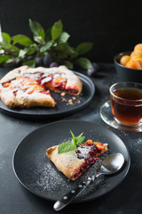 Tasty fall pie galette with plum and apricot on black table.