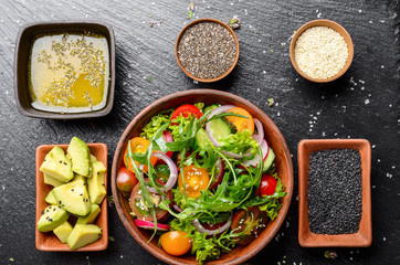 Top view at Clay dish with vegetable salad of lettuce, cherry tomatoes, radish, cucumber, onion and basil on slate tray