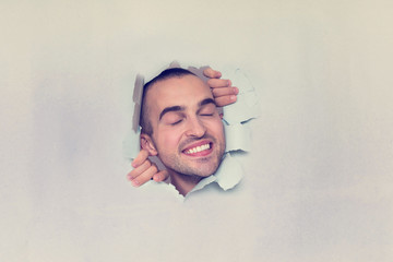 Happy man making hole in paper, smiling with closed eyes, portrait, blue background, copy space