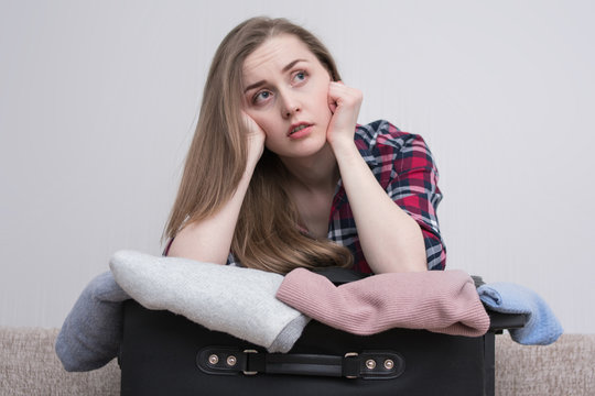 Young pensive woman with overstuffed suitcase in bed travel suitcase, sad looking to the side, close up