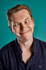 Close-up portrait of a ginger guy in navy t-shirt posing on blue background. Sincere emotions.