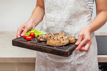 Woman holds a tray with tomatoes, grilled meat, lettuce and scattered spices, closeup