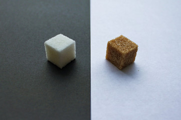 Close-up of the confrontation: two pieces of sugar - refined white on a black background and cane sugar on a white background opposite each other