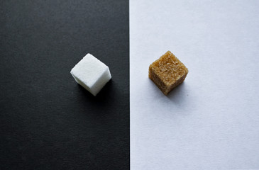 Top view of two pieces of sugar - refined white on a black background and cane sugar on a white background opposite each other