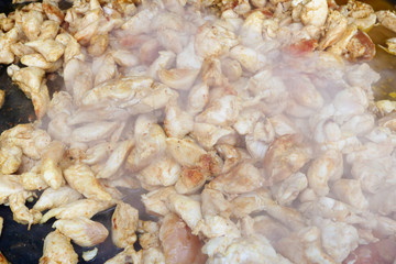 Fast street-food - smoked chicken slices  fried  in big iron black frying pan