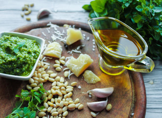 A bowl with pesto sauce and ingredients for its preparation: green Basil, Parmesan cheese, olive oil, pine nuts, salt and garlic on the background of aged board