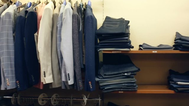 Variety of different suit jackets exposed on clothing rack in men clothes shop