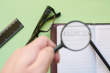 The inscription "Business" under a magnifying glass in the hands of a person. The concept of searching for business ideas. Flat lay