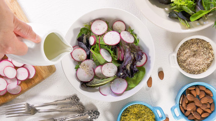  Herb Mix Salad with Fresh Organic Radish, Lettuces, Spinach, Some Seasoning, Almonds and Vegetable Oil. Close Up on White Background, Woman Hands