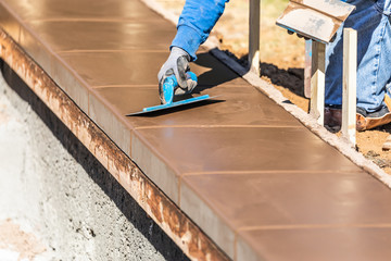 Construction Worker Using Trowel On Wet Cement Forming Coping Around New Pool