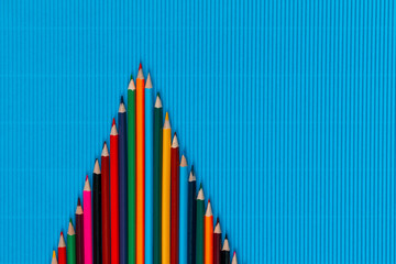 A bunch of crayons forming a triangle on a blue background, shot from above, arranged in the center.