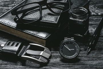 Business concept background. Black leather book, inkwell with a quill pen, wallet, eye glasses and a hand watch on a black wooden table.