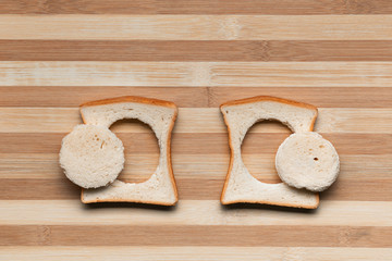 Two slices of bread with their centers cut on a brown table, shot from above.