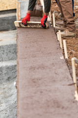 Construction Workers Pouring And Leveling Wet Cement Into Wood Framing