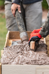 Construction Workers Pouring And Leveling Wet Cement Into Wood Framing