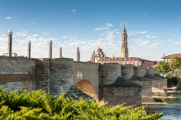 View of the medieval stone bridge of Zaragoza (Puente de Piedra) over the river Ebro, with the tower of the cathedral of La Seo in the background.