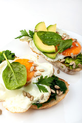 Fried eggs on a toasts bread with avocado, spinach and seeds on a white plate on the white background.