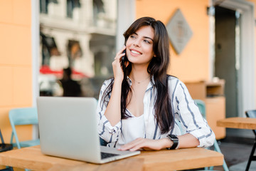 smiling woman uses laptop sitting near cafe