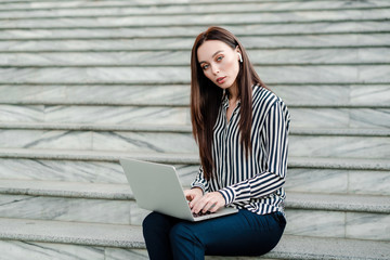 woman with laptop sitting on stairs in the city